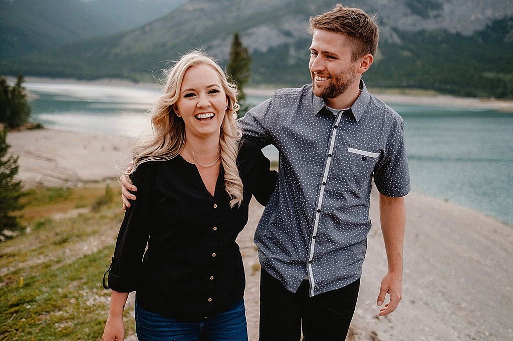 Happy couple walking along mountain lakeside path while laughing together.