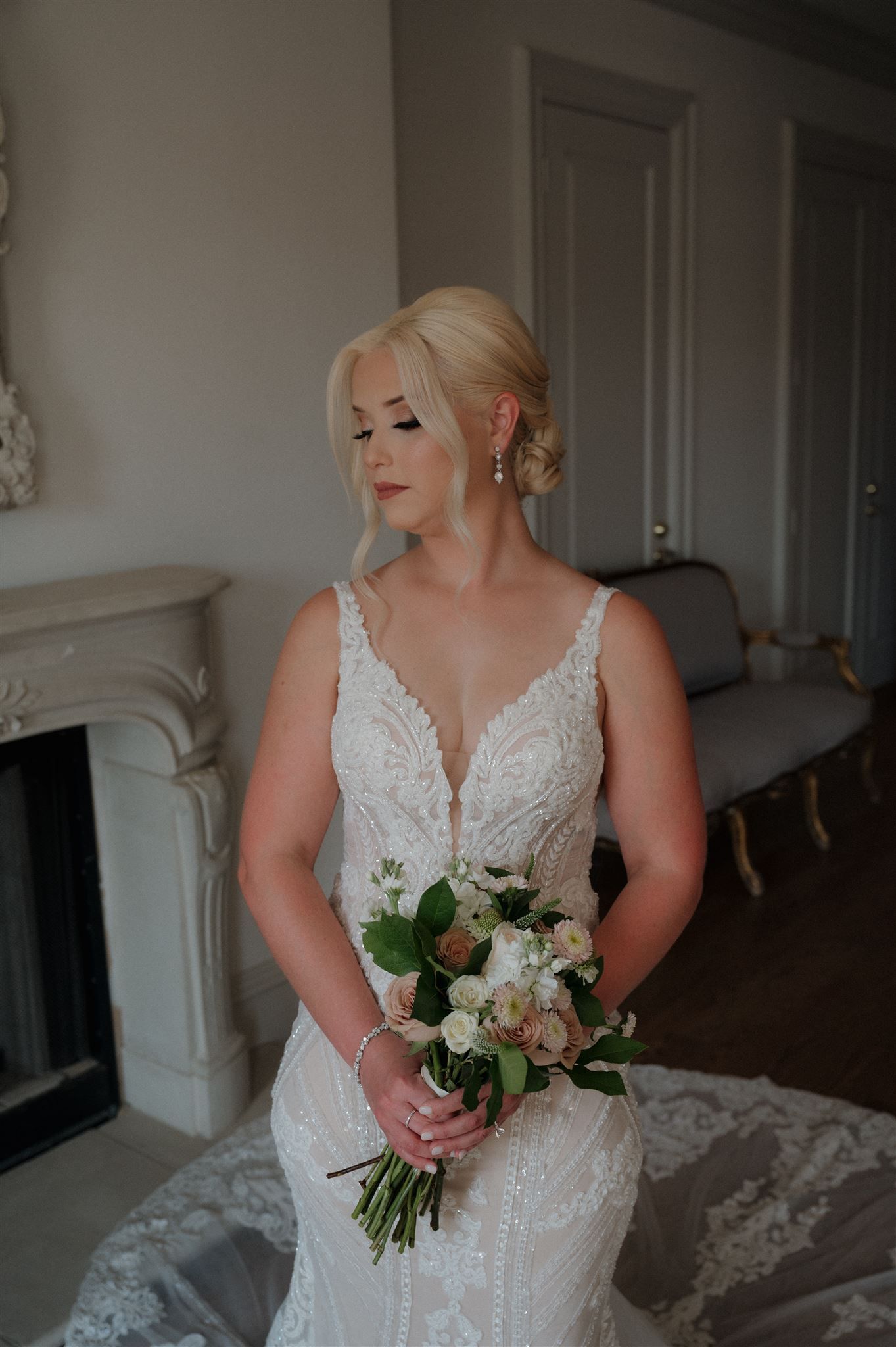 Elegant bridal portrait featuring lace dress and romantic bouquet in classic room setting.