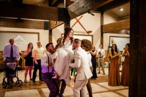 Wedding guests dance and celebrate in a rustic venue with exposed wooden beams.