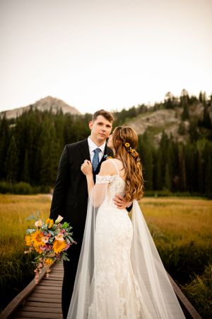 Wedding portraits on wooden boardwalk with mountain peaks and wildflower bouquet in view.