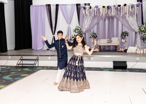 Elegant indoor wedding reception setup with purple draping and white decor.
