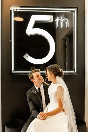 Wedding couple sharing an intimate moment against a dark wall with illuminated number decor.