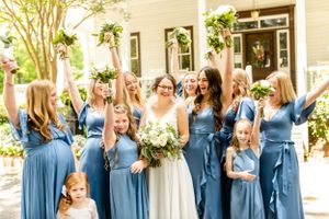 Wedding party members in coordinating blue dresses standing in front of a white building.