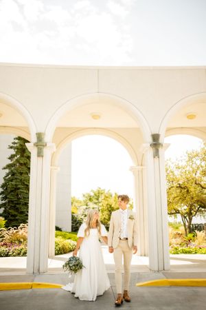 Elegant white archways frame a couple in wedding attire on a sunny day.