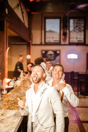 Wedding party members in white attire laugh and celebrate together during reception festivities.
