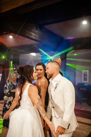 Wedding guests dance together under colorful disco lights at an indoor reception celebration.