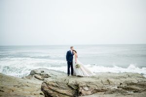 A couple shares an intimate moment on rocky coastal cliffs overlooking the ocean.