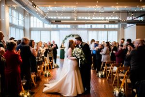 Wedding ceremony in a spacious venue with string lights and large windows overlooking the celebration.