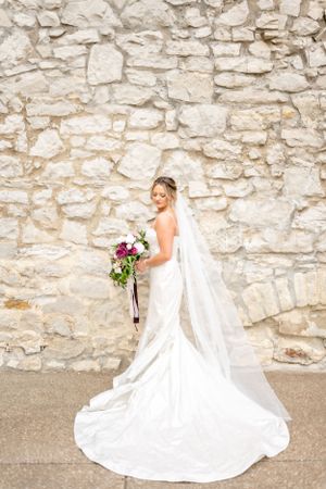 Elegant bridal portraits showing flowing white wedding dress against textured stone wall backdrop.