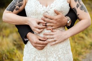 Close up of wedding couple's hands embracing, showing tattoos and lace dress details.