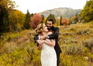 Joyful wedding embrace in autumn field with mountain scenery and fall foliage.