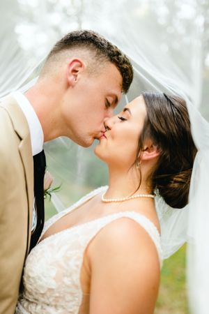 Intimate wedding portrait under flowing veil in dreamy outdoor setting.