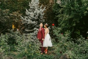 Wedding couple strolling through garden pathway surrounded by green foliage.