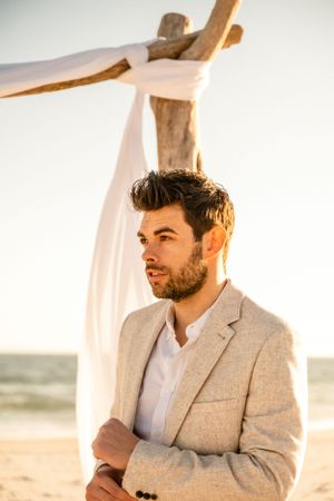 A beach wedding ceremony setup with driftwood arch and flowing white fabric against the ocean backdrop.