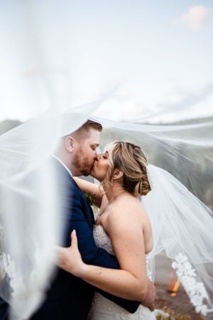 Romantic wedding couple embracing under flowing veil with soft dreamy lighting.