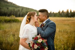 Romantic wedding couple embraces in golden mountain meadow at sunset.