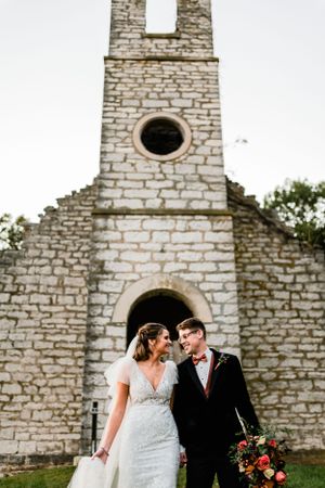 Wedding couple poses in front of historic stone church ruins.