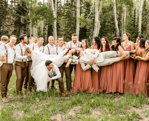 Large wedding party posed in forest setting with bridesmaids in dusty rose dresses.