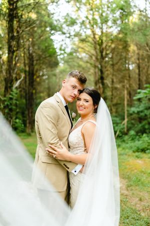 Wedding couple poses romantically in a lush green forest setting.