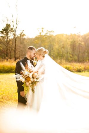 Newlyweds share an intimate moment in a sunlit field with flowing veil.