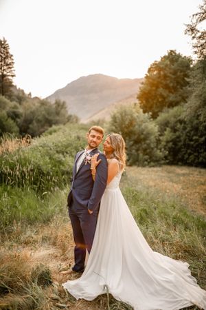 Wedding couple embraces in a mountainous landscape with flowing white dress.
