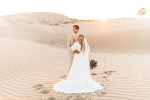 Ethereal bridal portraits on sand dunes during golden hour with flowing white dress.