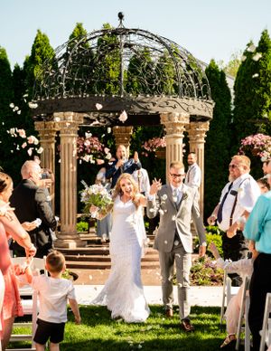 Wedding celebration under a garden gazebo with guests gathered around pillars and floral decorations.