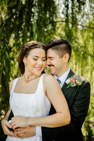 A tender moment between newlyweds under weeping willow trees in natural sunlight.