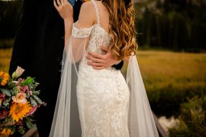Close up of bride's lace wedding dress details with flowing veil in mountain setting.