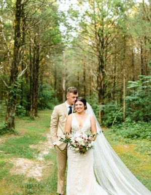 Wedding couple posing on a forest path with lush green trees and natural lighting.