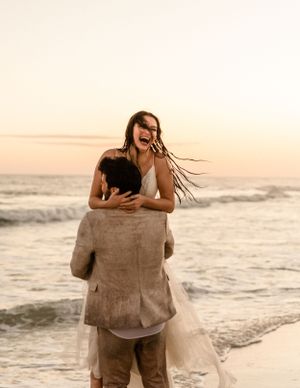 Couple sharing intimate moment on beach with waves and sunset in background.