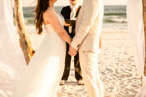 Beach wedding ceremony with guests gathered on sandy shore at sunset.