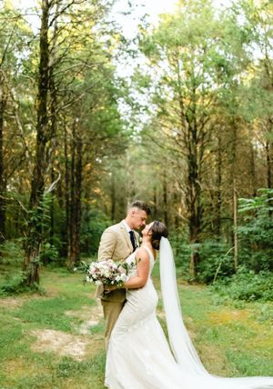 Newlyweds embrace in a serene forest setting with natural greenery.