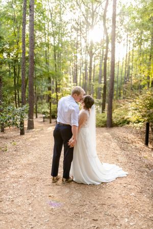 Romantic wedding photo series in a sunlit wooded area with pine trees.