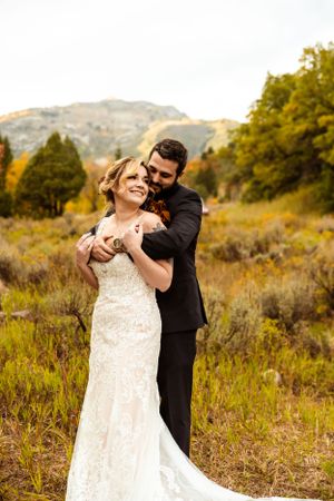 Intimate wedding moment captured in golden autumn field with mountain backdrop.