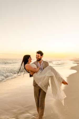 A romantic beach scene at sunset with a couple embracing in formal attire on the sandy shore.