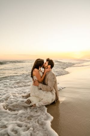 Wedding couple posing in ocean surf during golden hour photography session.