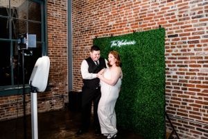 Wedding celebration against exposed brick wall with green hedge backdrop and ambient lighting.