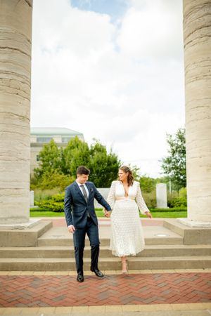 Romantic couple poses between elegant stone columns on a brick patio during a wedding photoshoot.
