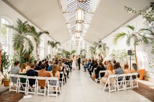 An elegant wedding venue with skylights, palm trees, and white chairs set up for a ceremony.