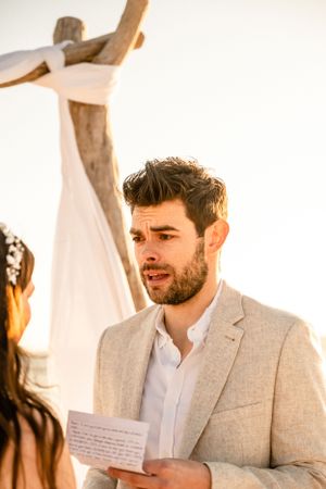 A beachside wedding ceremony with a rustic driftwood arch and white fabric decor.