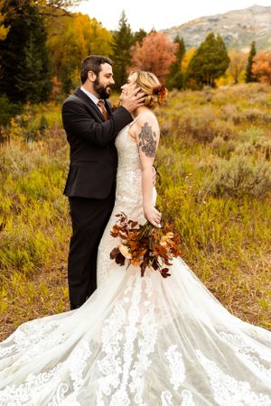 Romantic wedding portrait in autumn field with mountains and dramatic lace dress train.
