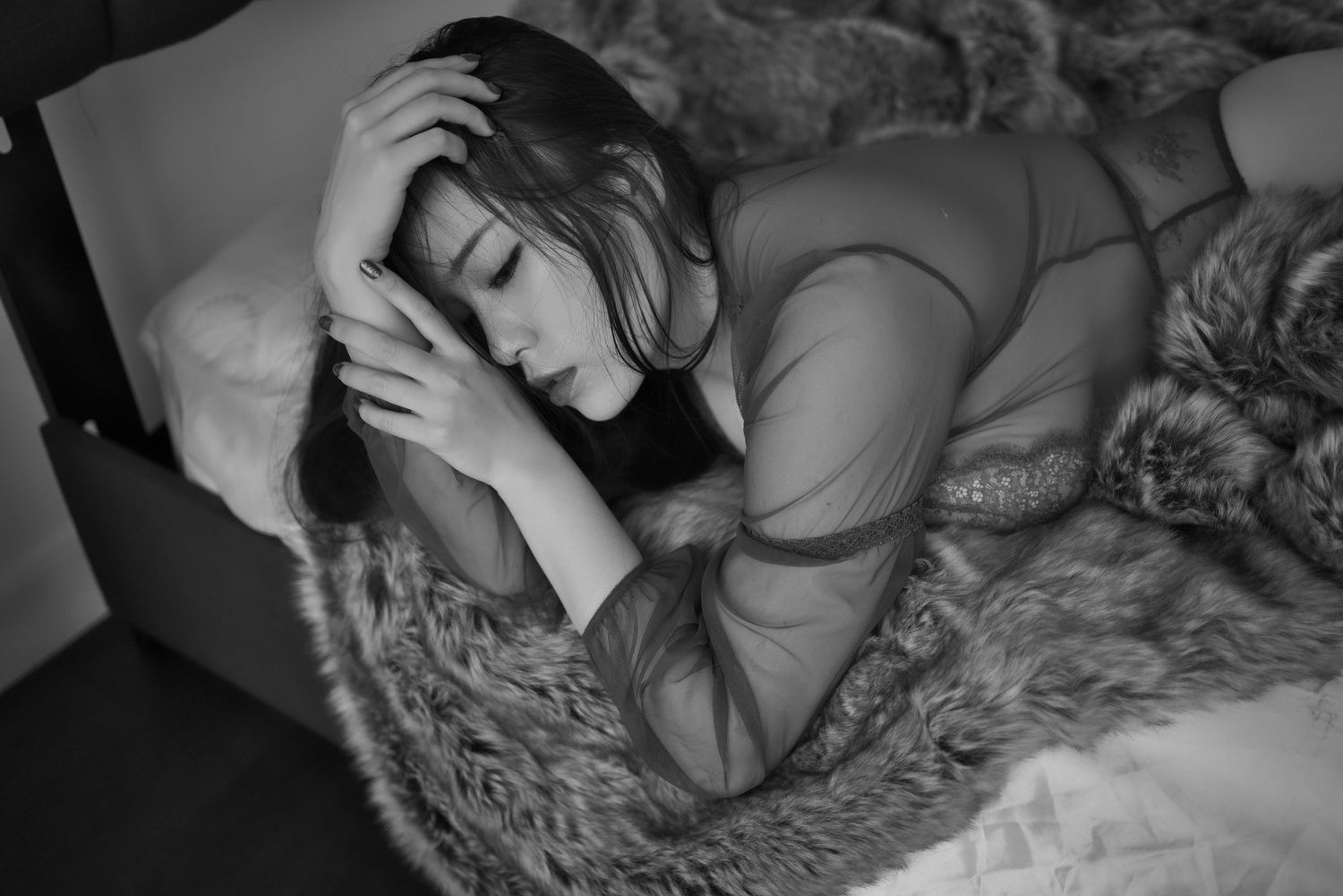 Moody black and white portrait of a person in intimate poses on plush fur bedding.