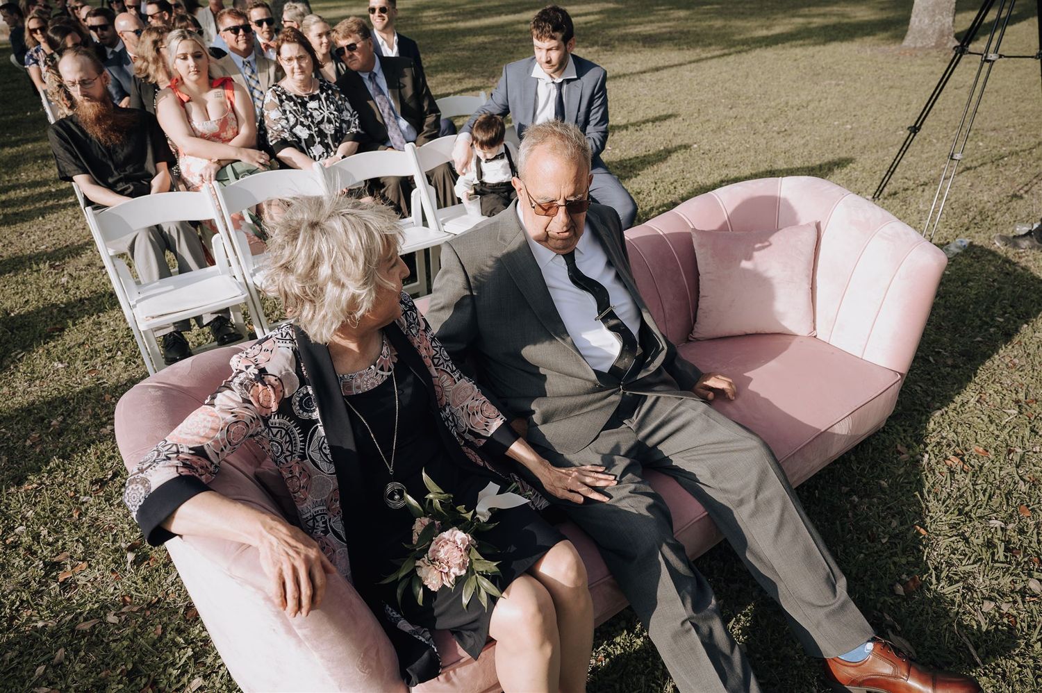Guests relaxing on a pink sofa during an outdoor wedding ceremony.