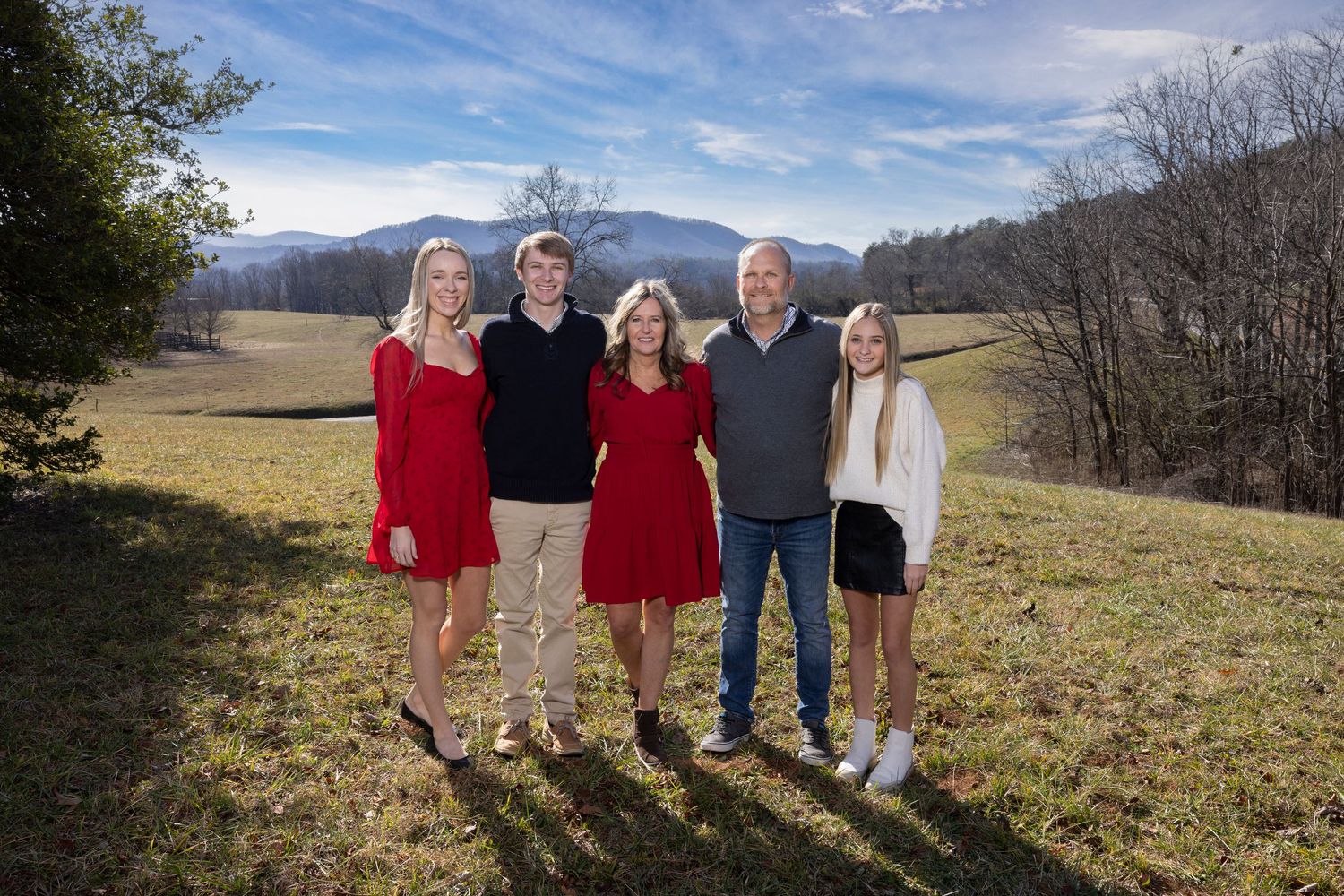 Group photo of five people standing together on grassy hillside with mountain landscape behind them.