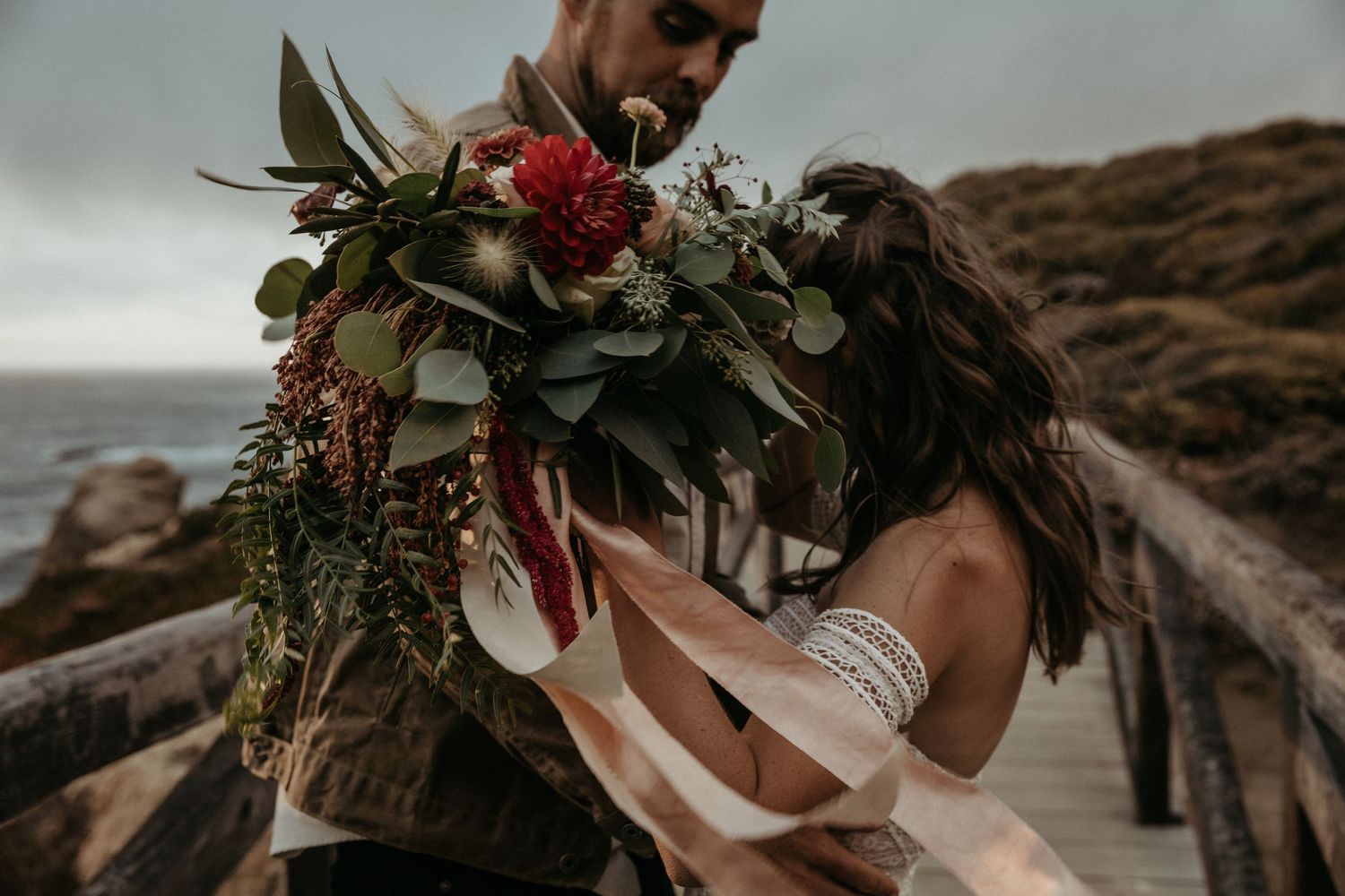 Romantic coastal moment with a bouquet featuring red flowers and eucalyptus leaves.