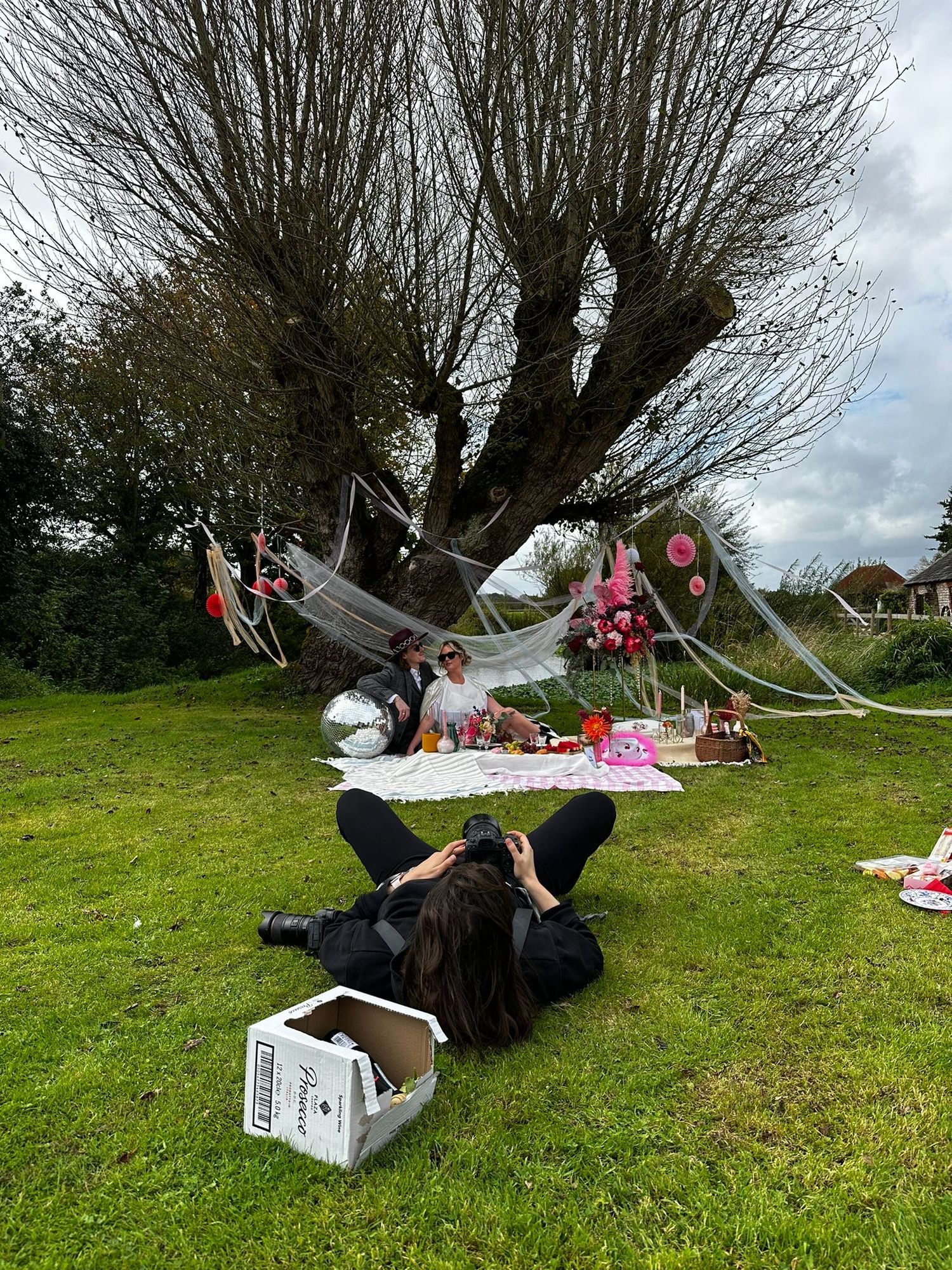 Amy laying on the floor shooting a couple on a blanket having a wedding picnic