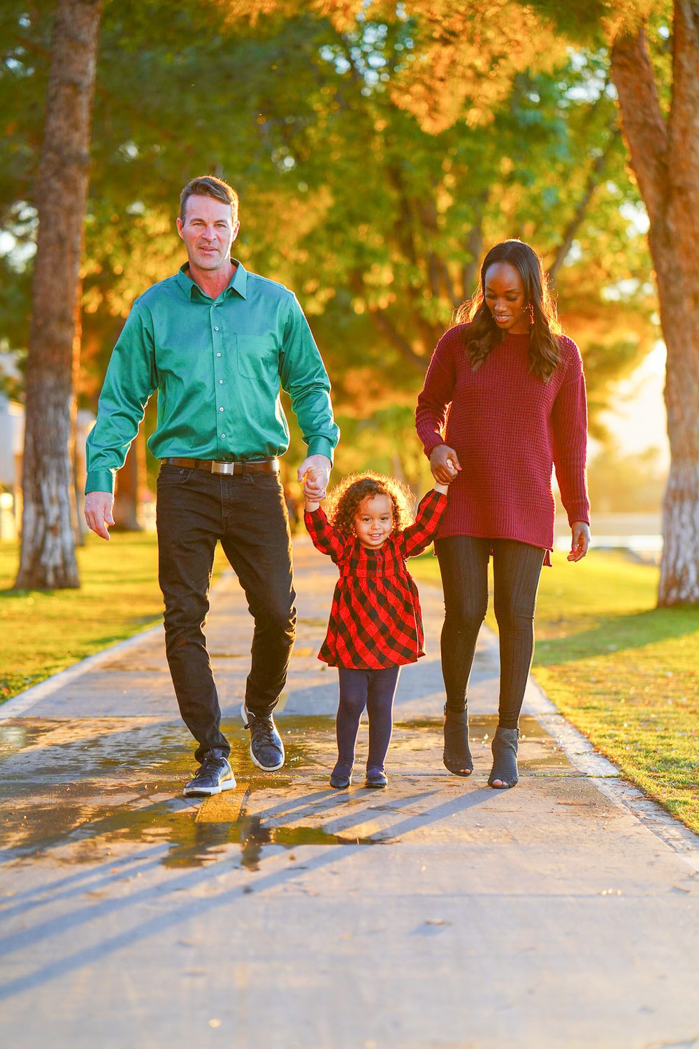 Family walking together on a sunlit path through a park during golden hour.