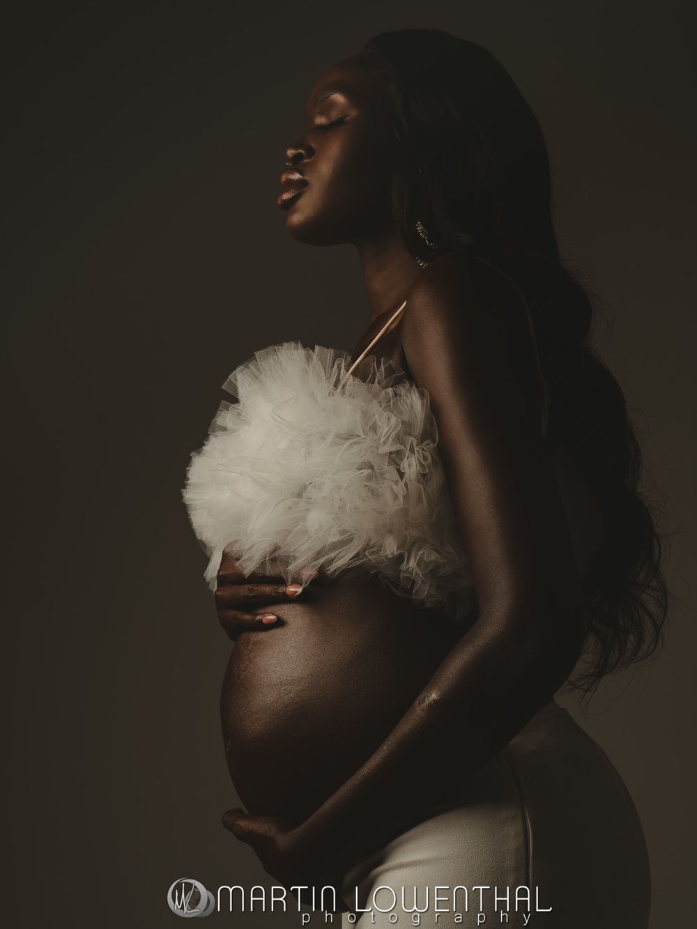 Dramatic maternity silhouette series with white tulle against dark background.
