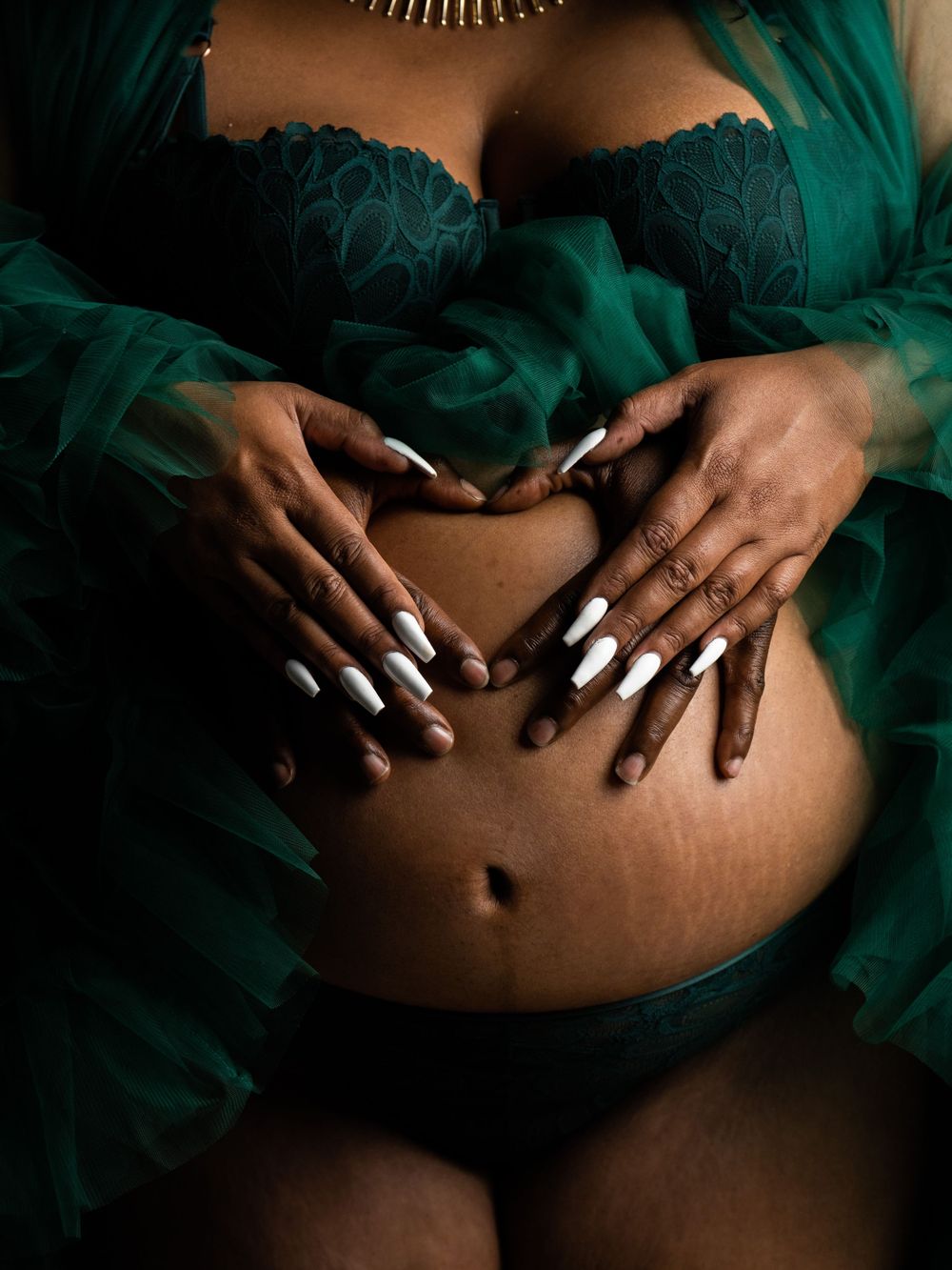 Artistic maternity photo series showing hands cradling a pregnant belly against emerald green fabric.